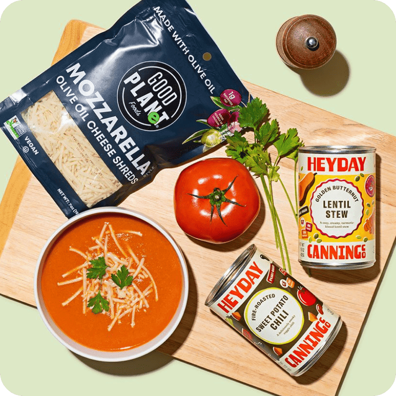 Heyday canned soup delivery with lentil stew and sweet potato chili beside a tomato soup bowl topped with Good Planet vegan mozzarella.