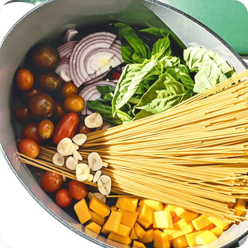 One-pot pasta delivery ingredients with spaghetti, cherry tomatoes, basil, red onion, garlic, and butternut squash ready to cook.