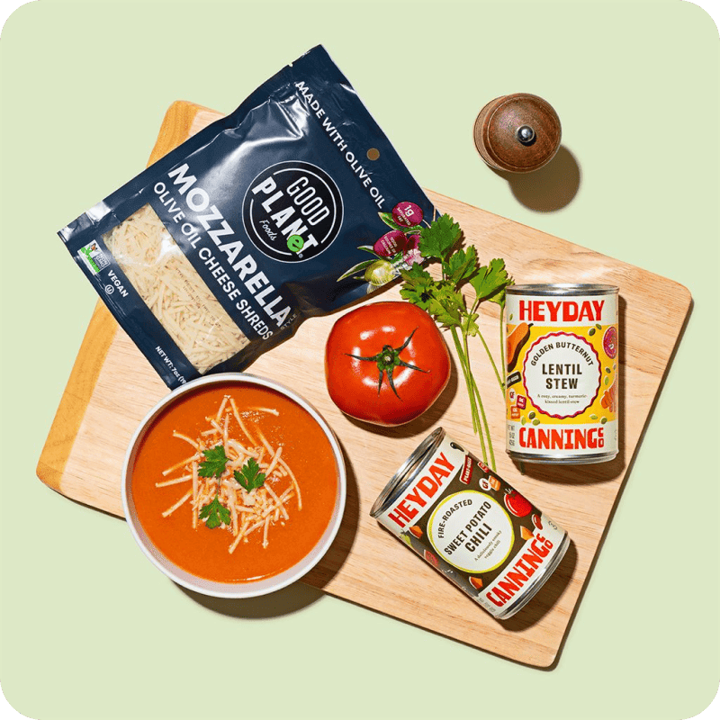 Gourmet soup delivery spread: tomato soup, mozzarella shreds, fresh tomato, and Heyday Canning Co. lentil stew and chili.
