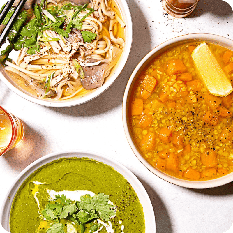 Three gourmet soup delivery dishes: herb noodle soup, butternut lentil stew, and creamy green herb soup with cilantro.