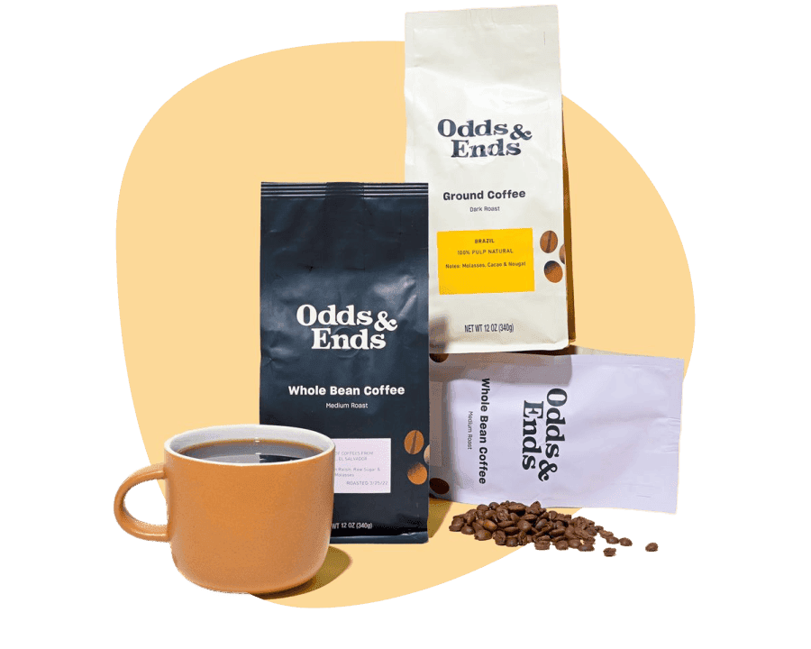 Order coffee beans online: Odds & Ends whole bean and ground coffee bags with beans scattered beside a coffee mug. 
