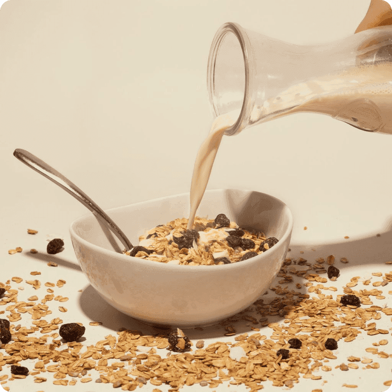 Organic almond milk pouring from a glass bottle into a bowl of cereal, delivered fresh to your door.